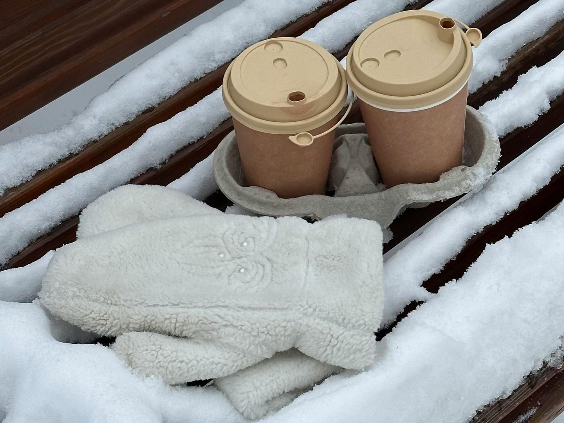 Warm knit gloves and coffee cups on a snow-covered bench in winter in Novokuznetsk, Russia.