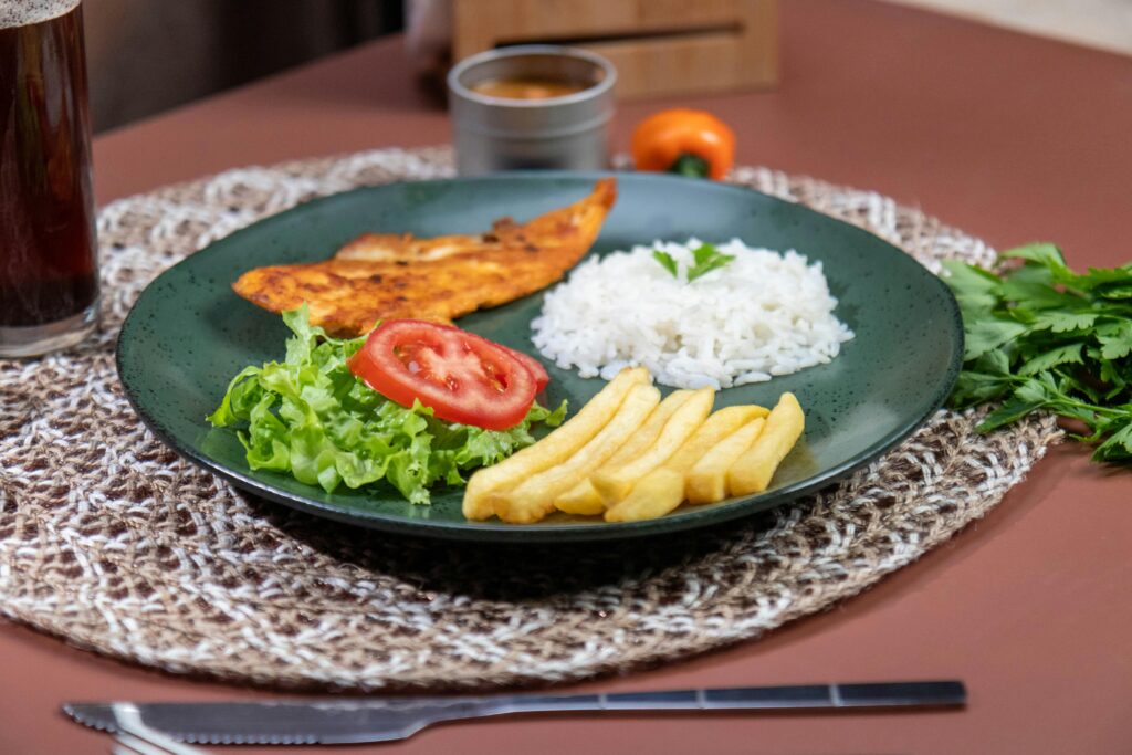 Appetizing meal featuring grilled fish, rice, and fries with fresh salad on a woven mat.