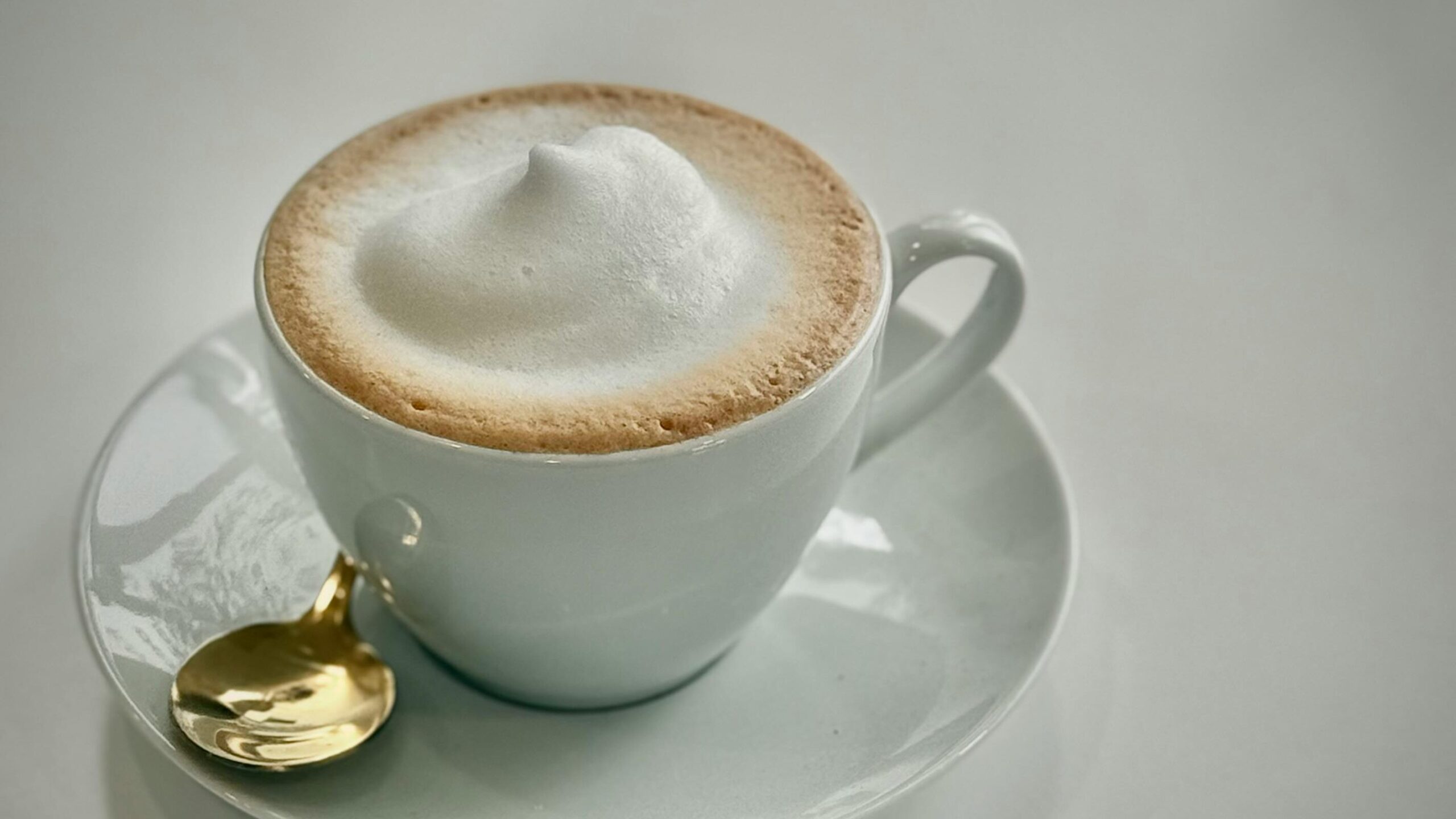 Golden spoon and frothy cappuccino in a white cup create a luxurious coffee setting.